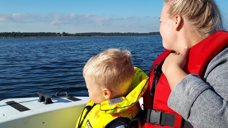 Barn och kvinna ombord på fritidsbåt vid Landön, iförda flytvästar.