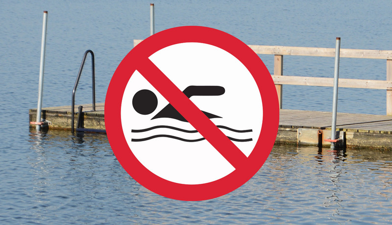 Badbrygga och vatten med ett förbudsmärke att det är olämpligt att bada