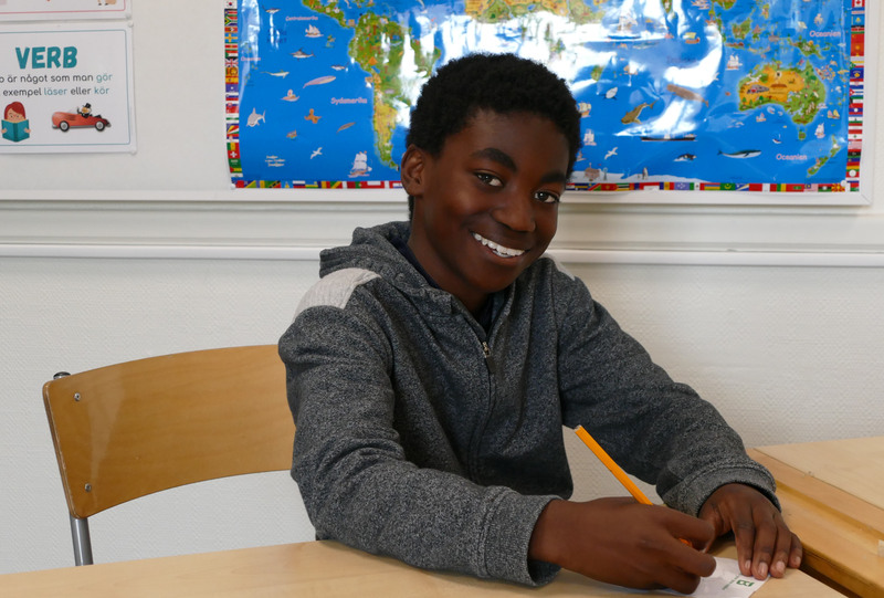 En elev sitter och skriver i sin skolbänk.