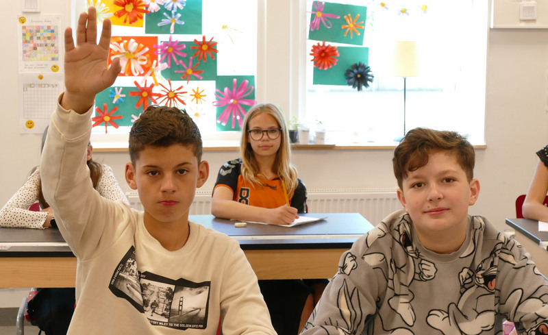 Bild på elever i klassrum där en elev räcker upp handen.